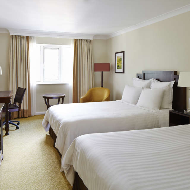 Twin guest room at Forest of Arden near Birmingham with two beds, desk, armchair and bright window with curtains