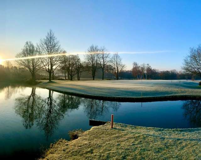 Sunrise over Forest of Arden golf course near Birmingham with frosty green, lake reflections and bare winter trees