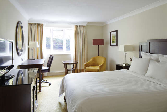 King guest room at Forest of Arden near Birmingham featuring bed, armchair, lamp and window with greenery view