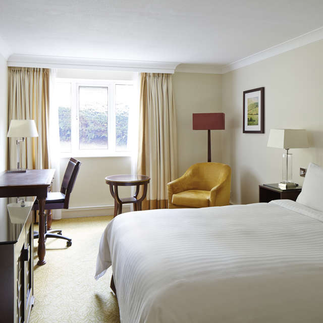 King guest room at Forest of Arden near Birmingham featuring bed, armchair, lamp and window with greenery view